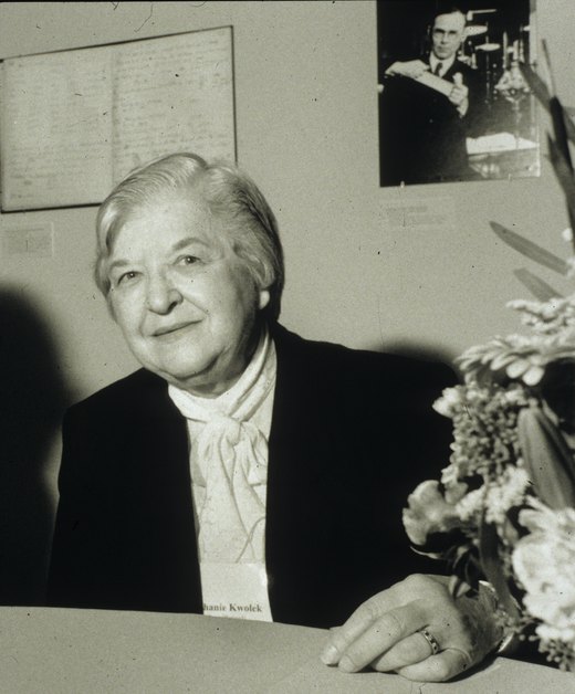 Photograph of Stephanie Kwolek later in life, seated at a table beside a bouquet of flowers, with a name card in front of her.